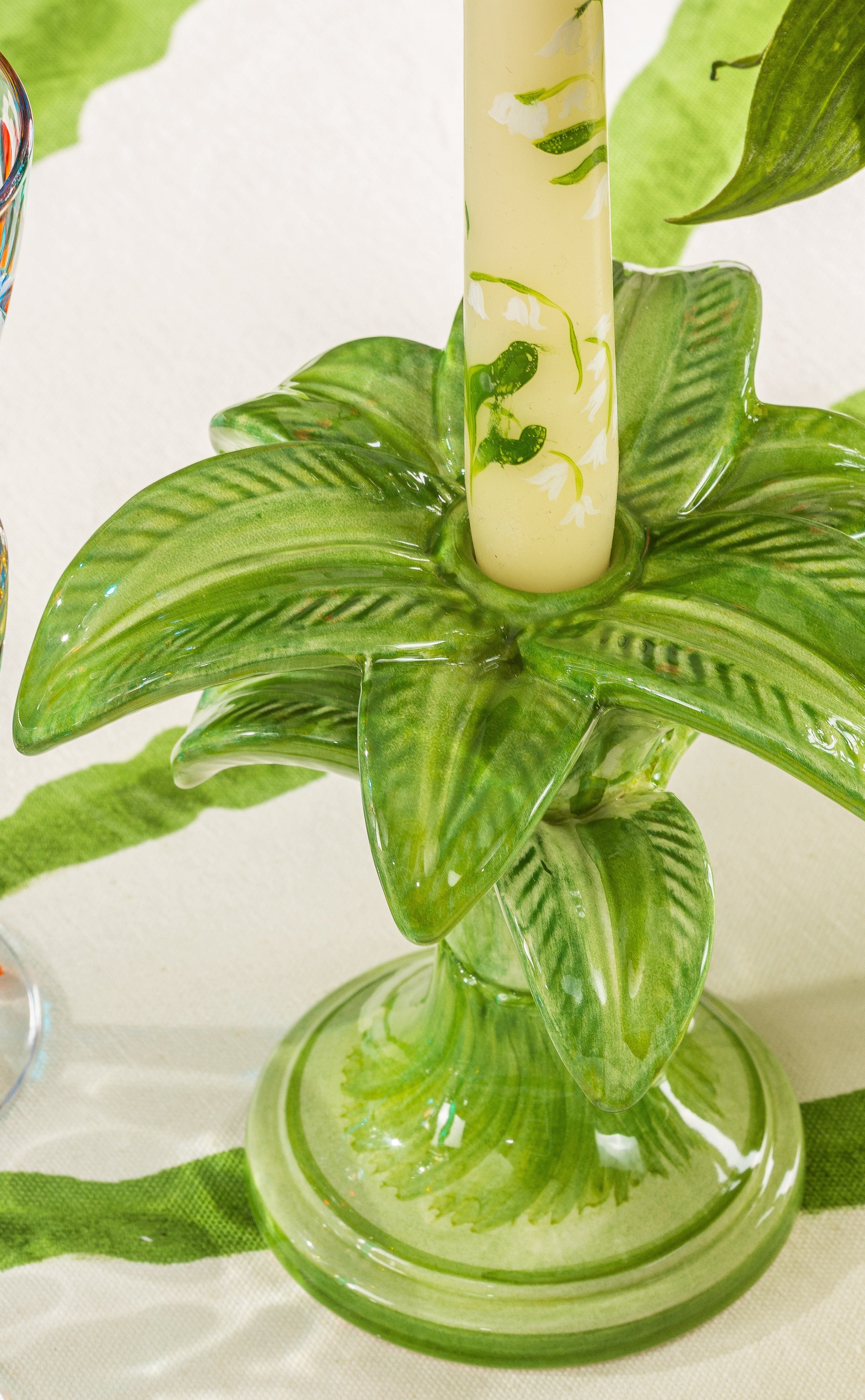 Nina Campbell ceramic small palm candlestick holder painted in green with a candle on a table