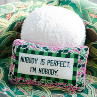 Nina Campbell Needlepoint Cushion Nobody is Perfect against a white pillow and colourful green cushion