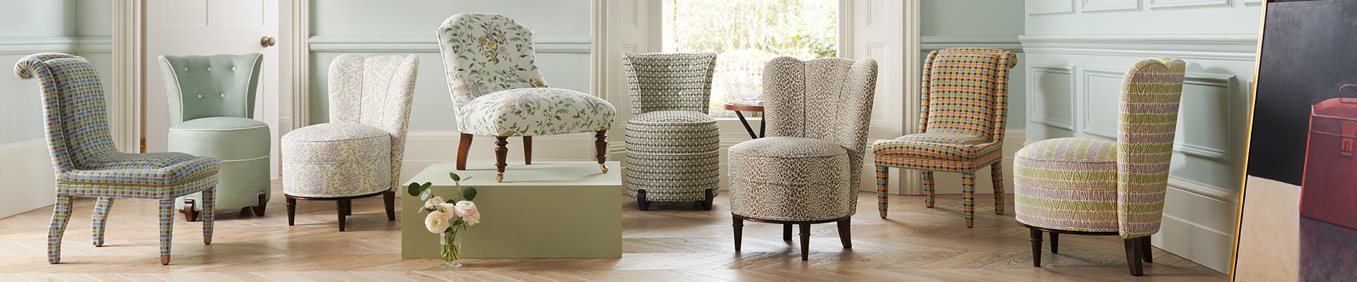 collection of small upholstered chairs in different fabrics and patterns in a blue room with wood floors