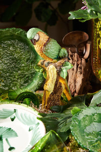 Nina Campbell ceramic parrot perched on branch in greens and yellows on table